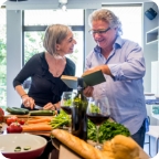 Elderly couple look at a cookbook and make dinner together.